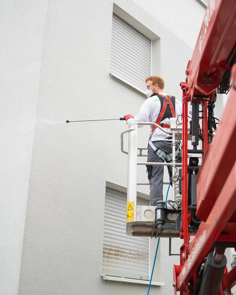 Mitarbeiter mit Sicherheitsgurt reinigt vom Hubsteiger aus eine Putzfassade mit der Teleskoplanze