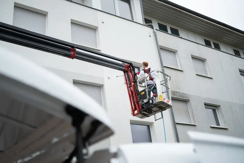 Mitarbeiter von FassadenProfis reinigt die Fassade eines Mehrfamilienhauses vom Hubsteiger aus